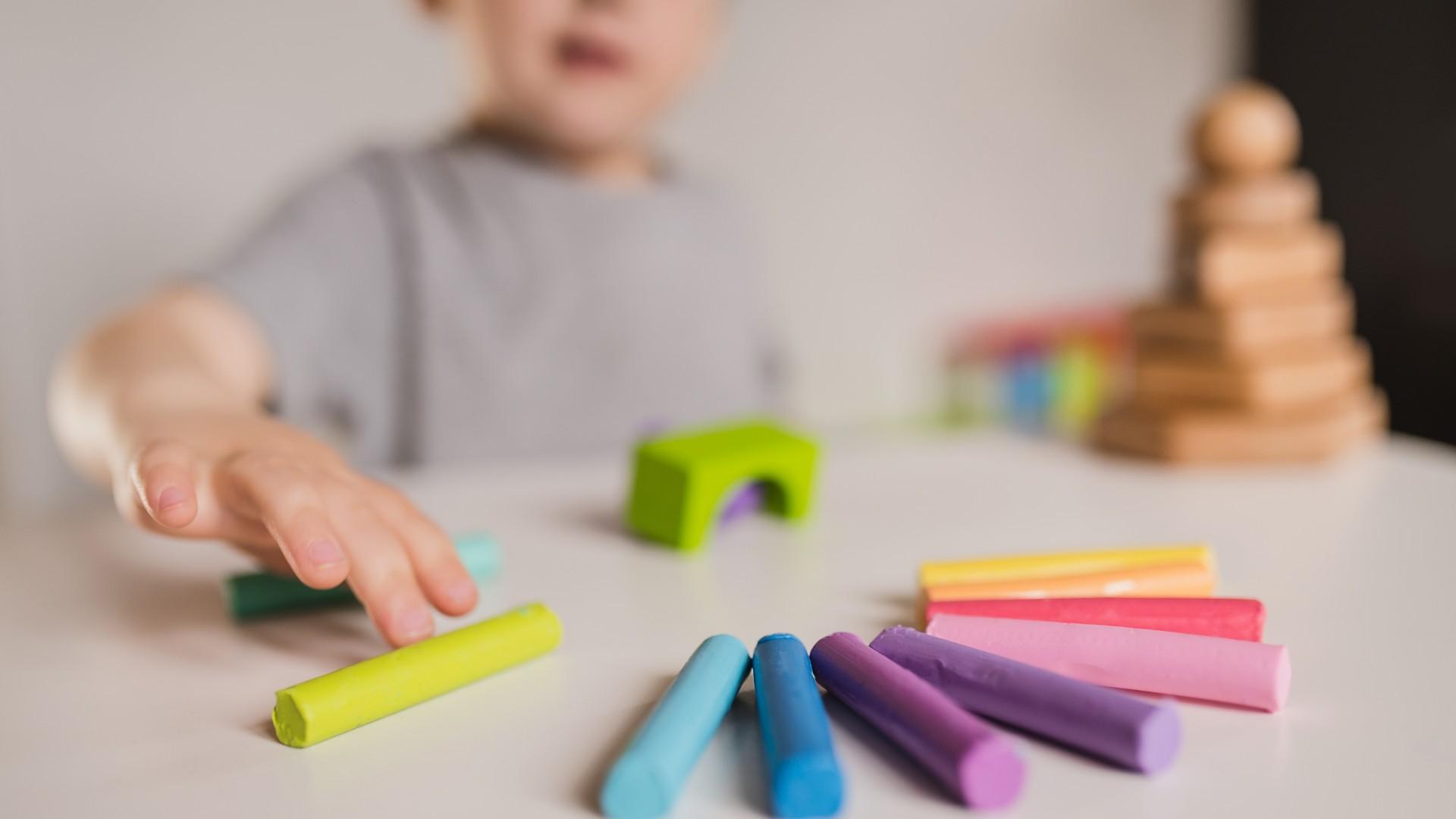 Bambino gioca con gessetti colorati su un tavolo.