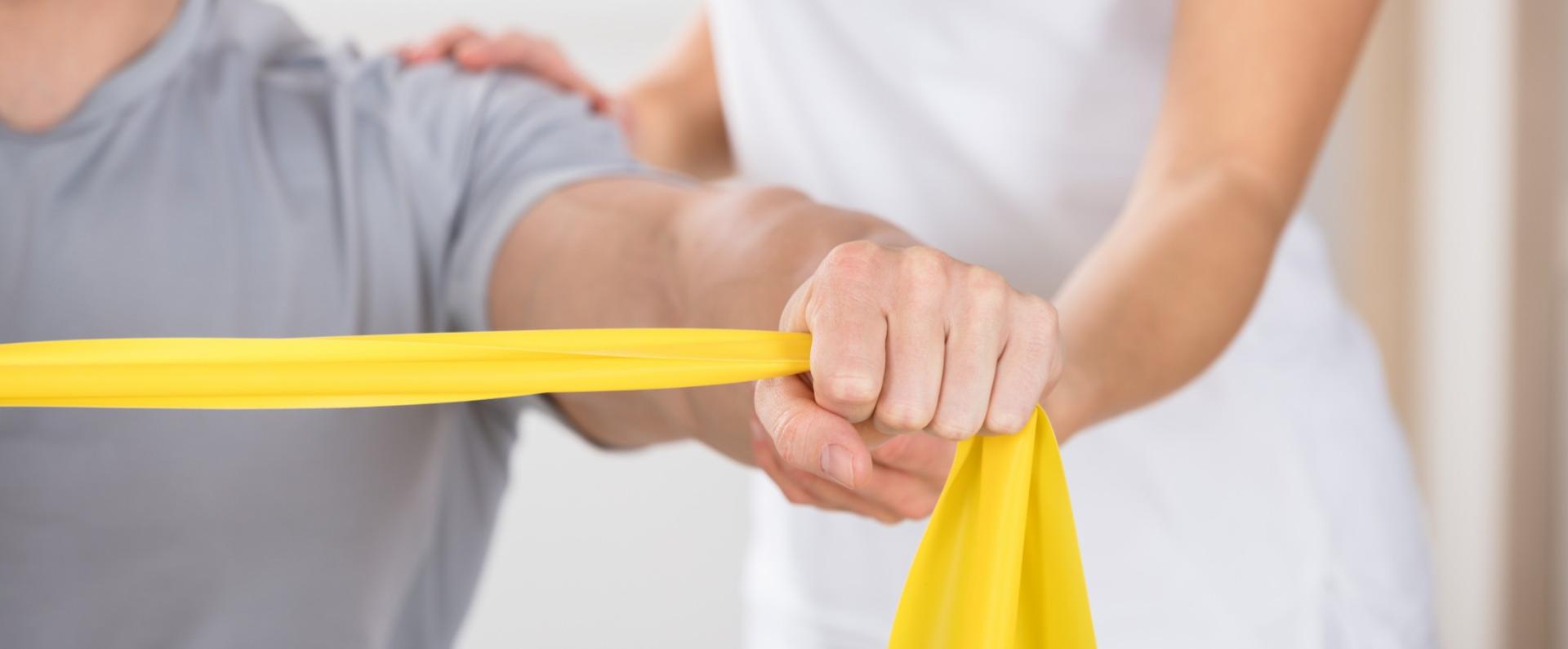 Esercizio di riabilitazione con fascia elastica gialla, assistito da un fisioterapista.