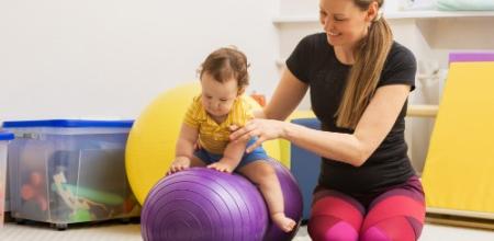 Donna gioca con un bambino su una palla fitness in una stanza luminosa.