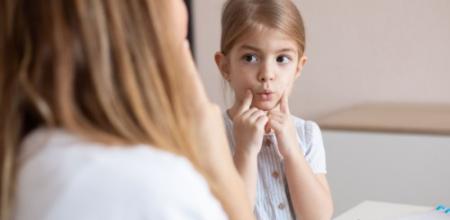 Bambina imita un adulto, toccandosi le guance durante un'attività educativa.