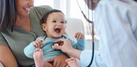 Medico controlla un bambino sorridente mentre la madre lo tiene in braccio.