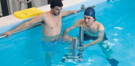 Due uomini in piscina, uno aiuta l'altro con esercizi di riabilitazione.