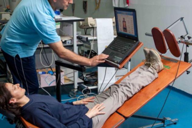 Persona su un lettino inclinato durante un esame medico con un tecnico al computer.